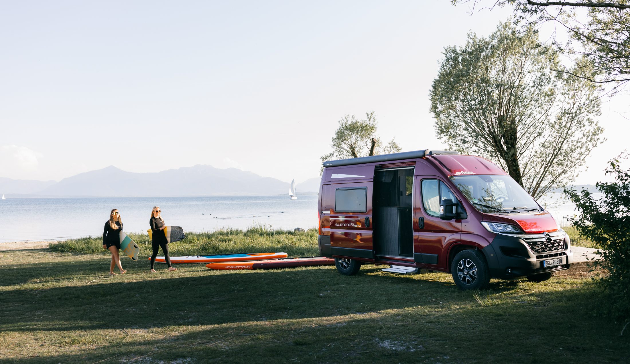 Zwei Freundinnen mit SUP-Boards am See neben ihrem Pössl Reisemobil